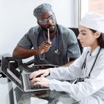 Dois médicos discutem o diagnóstico de uma paciente diante de um laptop em uma sala hospitalar.