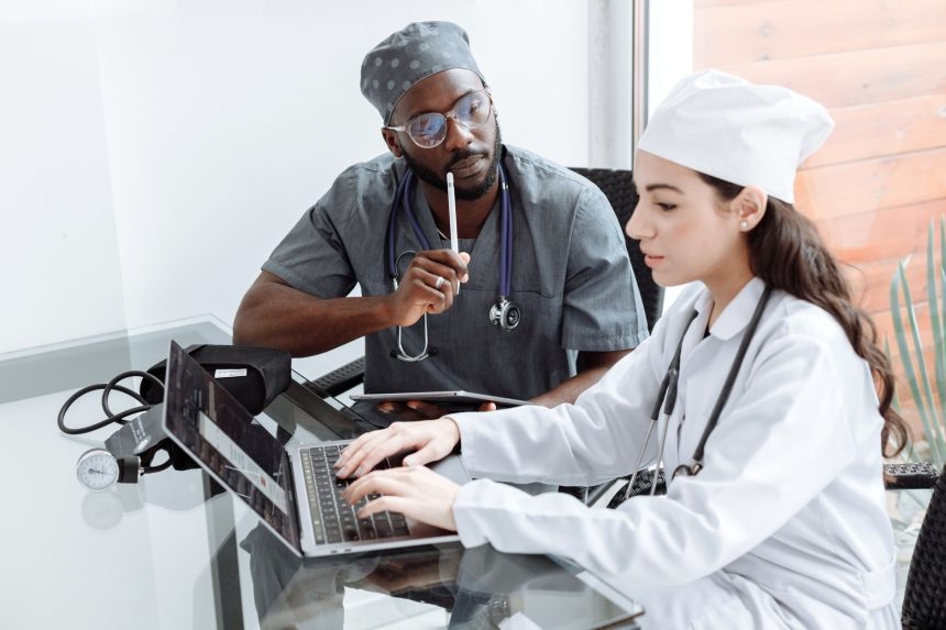 Dois médicos discutem o diagnóstico de uma paciente diante de um laptop em uma sala hospitalar.