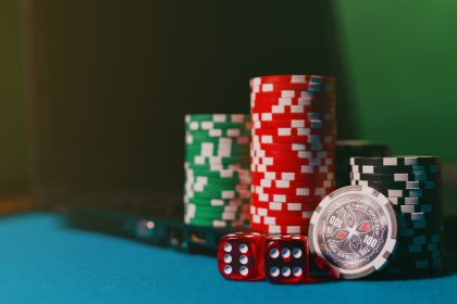 Laptop ao lado de fichas e dados sobre uma mesa de cassino, em referência às apostas online.