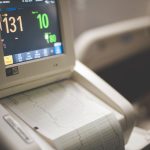 Close de um monitor hospitalar exibindo traçados de eletrocardiograma, frequência cardíaca e níveis de oxigênio.