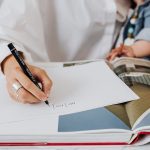 Mãe segura o bebê enquanto escreve em um caderno em ambiente interno.