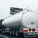 Caminhão-tanque transporta combustível por uma rodovia, visto por trás.