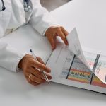 Profissional de saúde analisa relatórios de pacientes com uma prancheta em um consultório.
