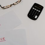 Documentos financeiros marcados como “pago” e “vencido” ao lado de uma calculadora e óculos.