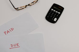 Documentos financeiros marcados como “pago” e “vencido” ao lado de uma calculadora e óculos.