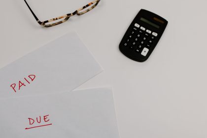 Documentos financeiros marcados como “pago” e “vencido” ao lado de uma calculadora e óculos.