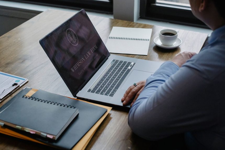 Pessoa usa um notebook sobre uma mesa com documentos e uma xícara de café.